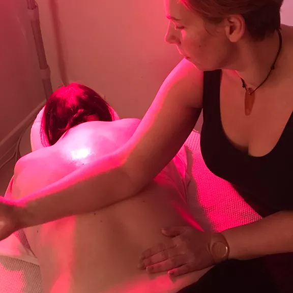 Een vrouw geeft een ontspannende massage onder warm rood licht, met focus op de rug van de persoon die wordt behandeld.