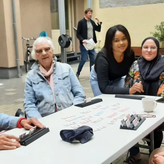 Een groep mensen die samen op een terras zitten en Rummikub spelen